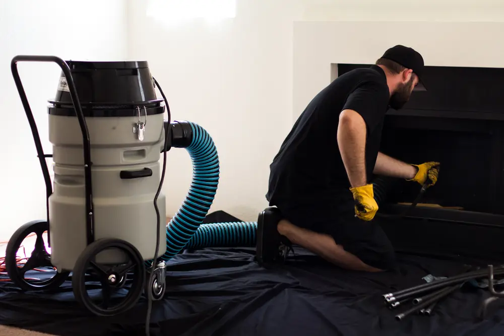 Technician cleaning a fireplace with a vacuum and drop cloth